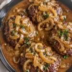 Cast iron skillet filled with Cracker Barrel copycat hamburger steaks smothered in rich homemade onion gravy with caramelized onions on a marble countertop.