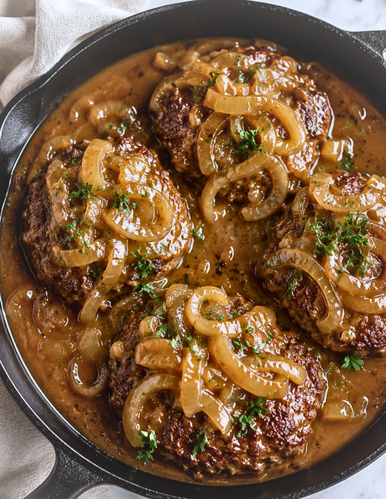 Cast iron skillet filled with Cracker Barrel copycat hamburger steaks smothered in rich homemade onion gravy with caramelized onions on a marble countertop.