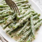 Fork lifting creamy Boursin green beans coated in garlic and herb cheese sauce