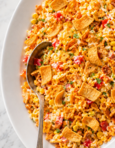 Easy corn chip salad with sweet corn, cheddar cheese, red bell pepper, creamy dressing, and crunchy whole Fritos on a white platter.