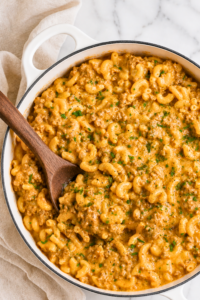 Easy homemade one-pan cheeseburger Hamburger Helper with ground beef, elbow macaroni, and creamy cheddar cheese sauce in a white enamel pot.