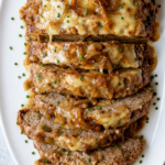 Sliced French onion meatloaf topped with melted cheese, caramelized onions, chives, and savory onion gravy.