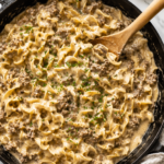 Creamy one pan Amish style beef and noodles made with tender egg noodles, seasoned ground beef, and a rich homemade gravy in a cast iron skillet topped with fresh chopped chives.