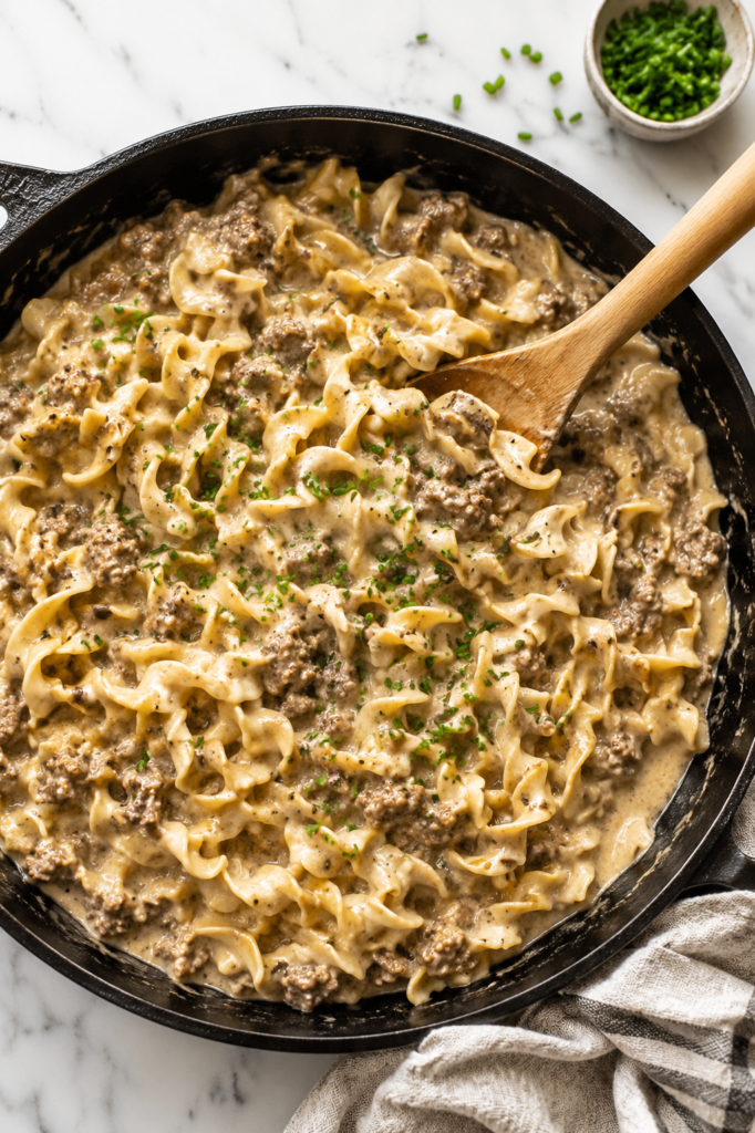 Creamy one pan Amish style beef and noodles made with tender egg noodles, seasoned ground beef, and a rich homemade gravy in a cast iron skillet topped with fresh chopped chives.