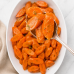 Serving spoon lifting orange juice glazed carrots from a white platter