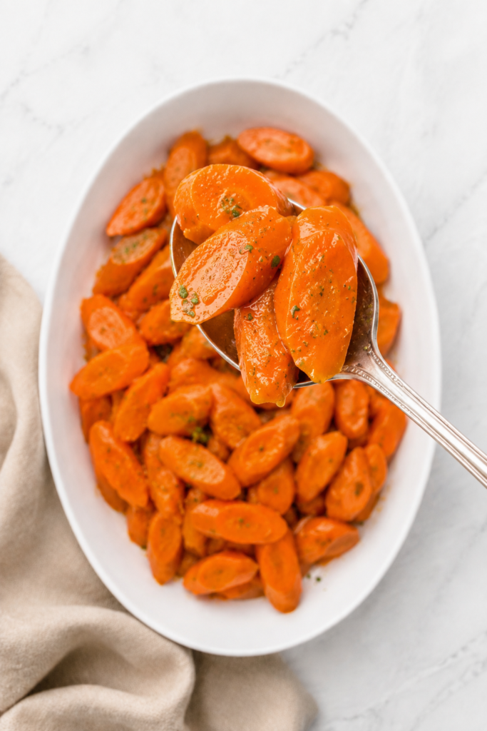 Serving spoon lifting orange juice glazed carrots from a white platter