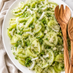 Fresh pickled green tomato salad with sliced green tomatoes, sweet onions, fresh dill, and tangy vinaigrette served on a white platter with wooden salad servers.