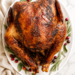 Crispy deep-fried Thanksgiving turkey on a white platter garnished with fresh herbs and cranberries.