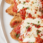 Better than Olive Garden chicken parmigiana with crispy breaded chicken, marinara sauce, and melted mozzarella on a white platter.