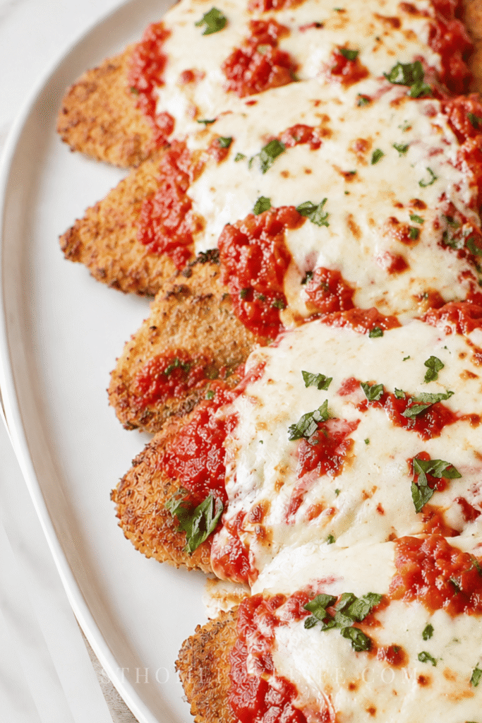 Better than Olive Garden chicken parmigiana with crispy breaded chicken, marinara sauce, and melted mozzarella on a white platter.