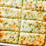 Homemade cheesy zucchini garlic bread cut into breadsticks and topped with melted mozzarella, Parmesan, garlic, and fresh parsley.