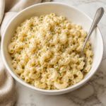 Creamy garlic macaroni salad with Romano cheese, black pepper and parsley served in a white bowl on a marble counter.