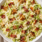 Creamy shaved Brussels sprout Caesar salad topped with crispy bacon, Parmesan cheese, golden croutons, and black pepper in a white bowl.