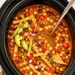 Crockpot vegetarian tortilla soup with beans, corn, tomatoes, avocado and crispy tortilla strips in a black slow cooker
