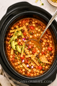Crockpot vegetarian tortilla soup with beans, corn, tomatoes, avocado and crispy tortilla strips in a black slow cooker