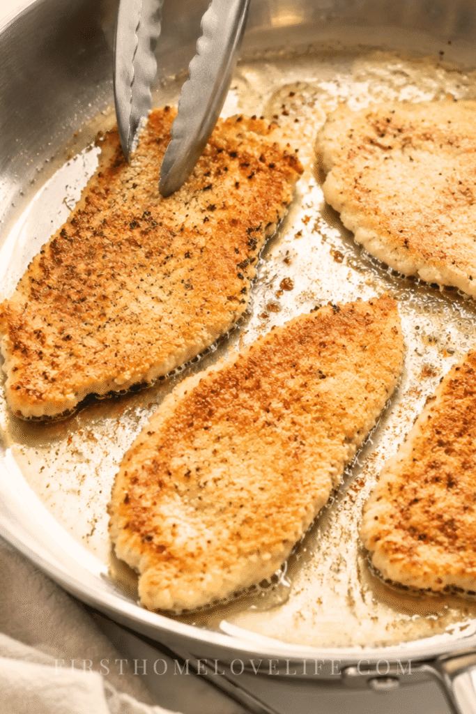 Thin breaded chicken cutlets frying until golden brown in a stainless steel pan for homemade chicken parmigiana.
