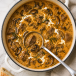 Creamy Hungarian steak and mushroom soup with paprika, sour cream and dill in a white enamel pot with a silver ladle.