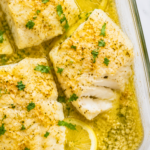 Flaky lemon garlic baked cod fillets with parsley and lemon slices in a glass baking dish.