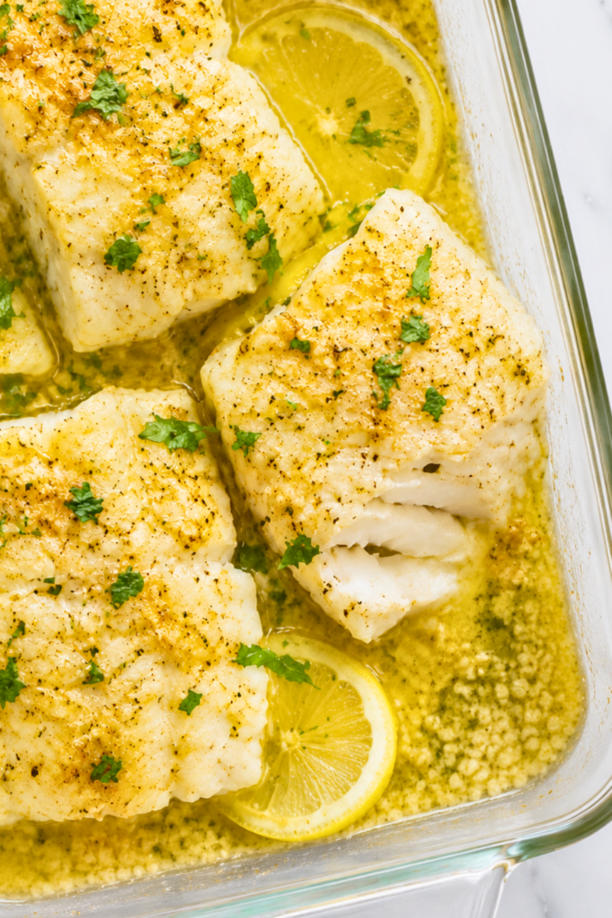 Flaky lemon garlic baked cod fillets with parsley and lemon slices in a glass baking dish.