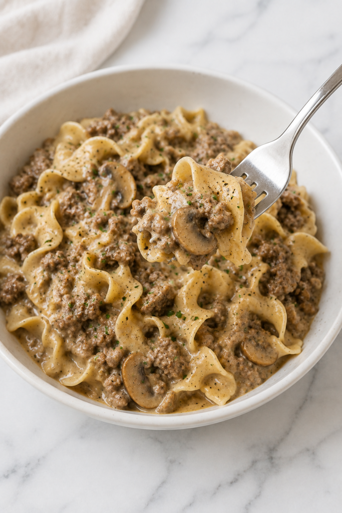 Fork lifting creamy Slow Cooker Hamburger Helper Beef Stroganoff with ground beef, mushrooms and egg noodles