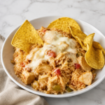 Creamy swim queso chicken and rice served in a white bowl with melted cheese, peppers, and tortilla chips.