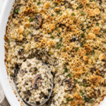 Creamy vintage rice and mushroom casserole with sliced mushrooms and a golden buttery cracker topping in a white oval baking dish.
