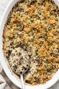 Creamy vintage rice and mushroom casserole with sliced mushrooms and a golden buttery cracker topping in a white oval baking dish.