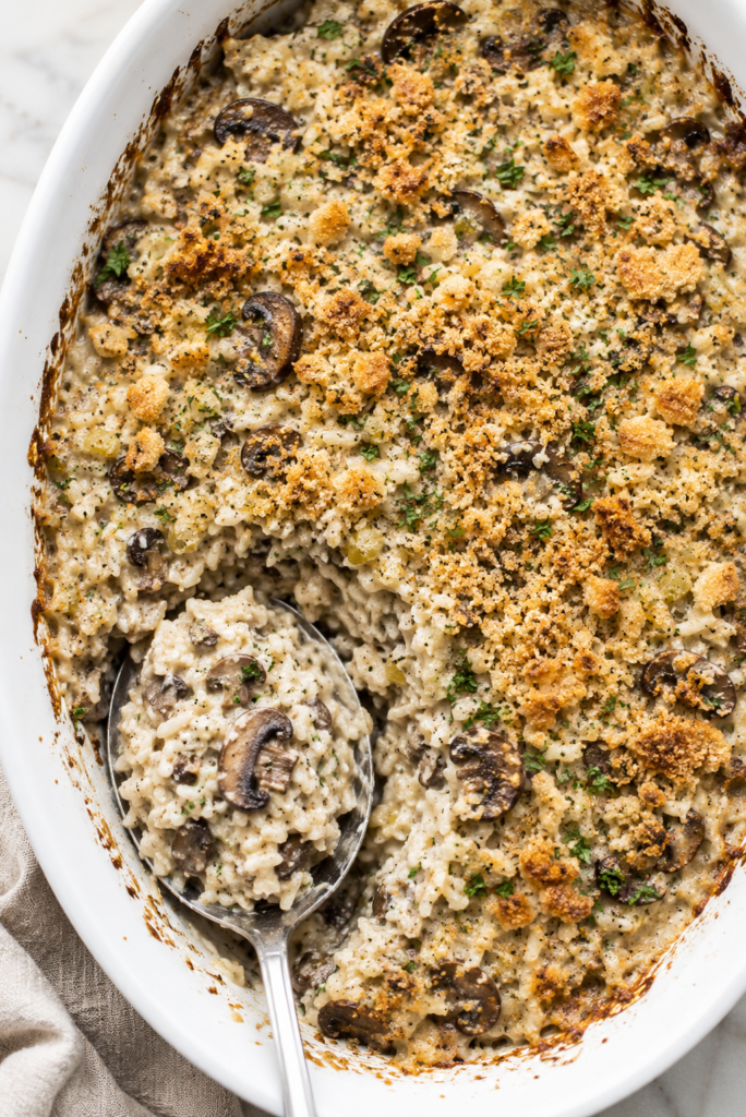 Creamy vintage rice and mushroom casserole with sliced mushrooms and a golden buttery cracker topping in a white oval baking dish.