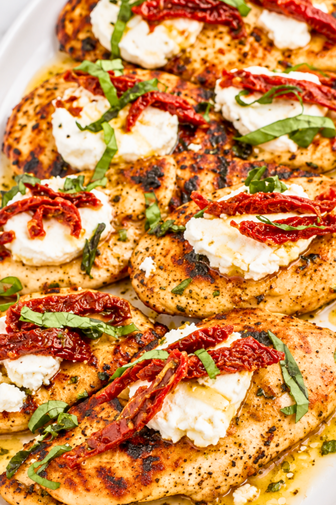 Carrabba’s Chicken Bryan copycat with grilled chicken, goat cheese, sun-dried tomatoes, basil, and lemon butter sauce on a white platter