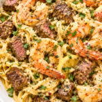 Close-up of cowboy butter shrimp and steak scampi with creamy linguine, seared steak bites, juicy shrimp, lemon slices, garlic, and fresh parsley