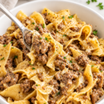 Creamy cowboy butter ground beef and egg noodles in a white bowl with garlic, Parmesan, black pepper, and parsley