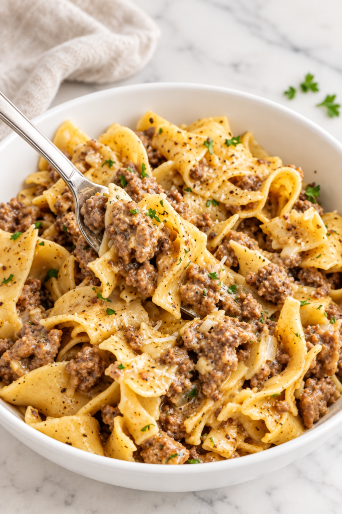 Creamy cowboy butter ground beef and egg noodles in a white bowl with garlic, Parmesan, black pepper, and parsley