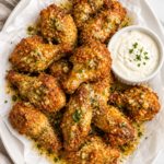 Crispy cowboy butter chicken wings drizzled with garlic lemon butter and served with ranch dressing on a white platter