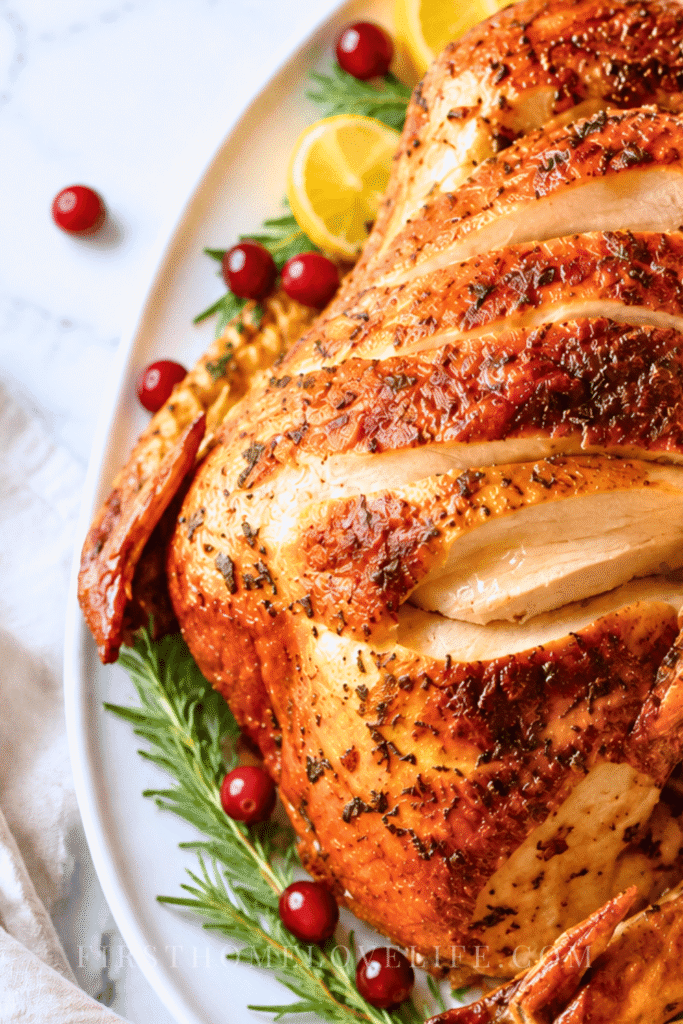Juicy dry brined Thanksgiving turkey with sliced breast meat, rosemary, lemon, and fresh cranberries on a white platter.