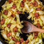 Overhead view of fried cabbage and bacon in a cast iron skillet with tender caramelized cabbage, onion, and crisp bacon pieces.
