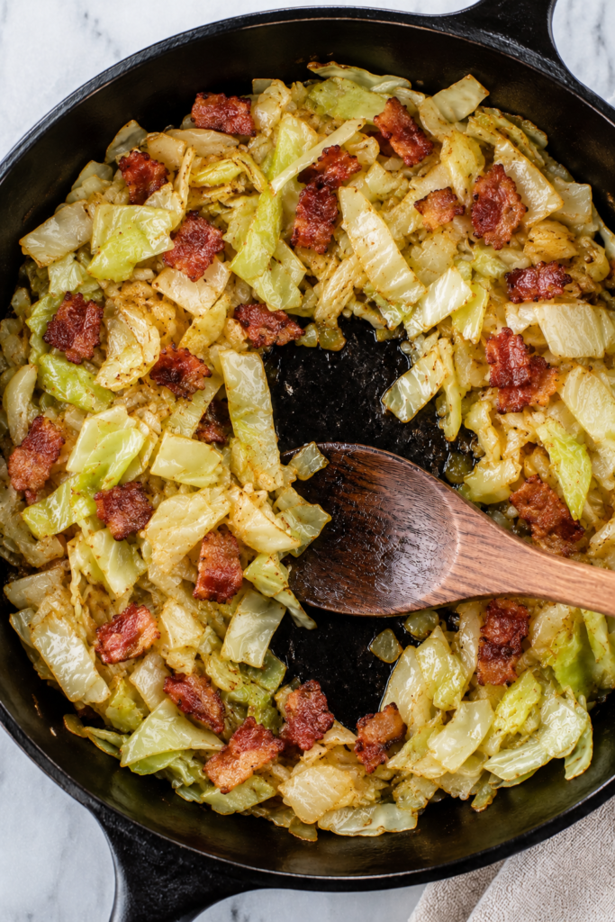 Overhead view of fried cabbage and bacon in a cast iron skillet with tender caramelized cabbage, onion, and crisp bacon pieces.