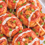 Fried Nashville hot chicken pinwheel smash skewers with ground chicken, ranch drizzle, chopped scallions, and spicy hot sauce.