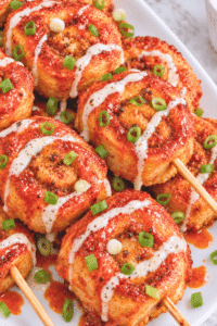 Fried Nashville hot chicken pinwheel smash skewers with ground chicken, ranch drizzle, chopped scallions, and spicy hot sauce.