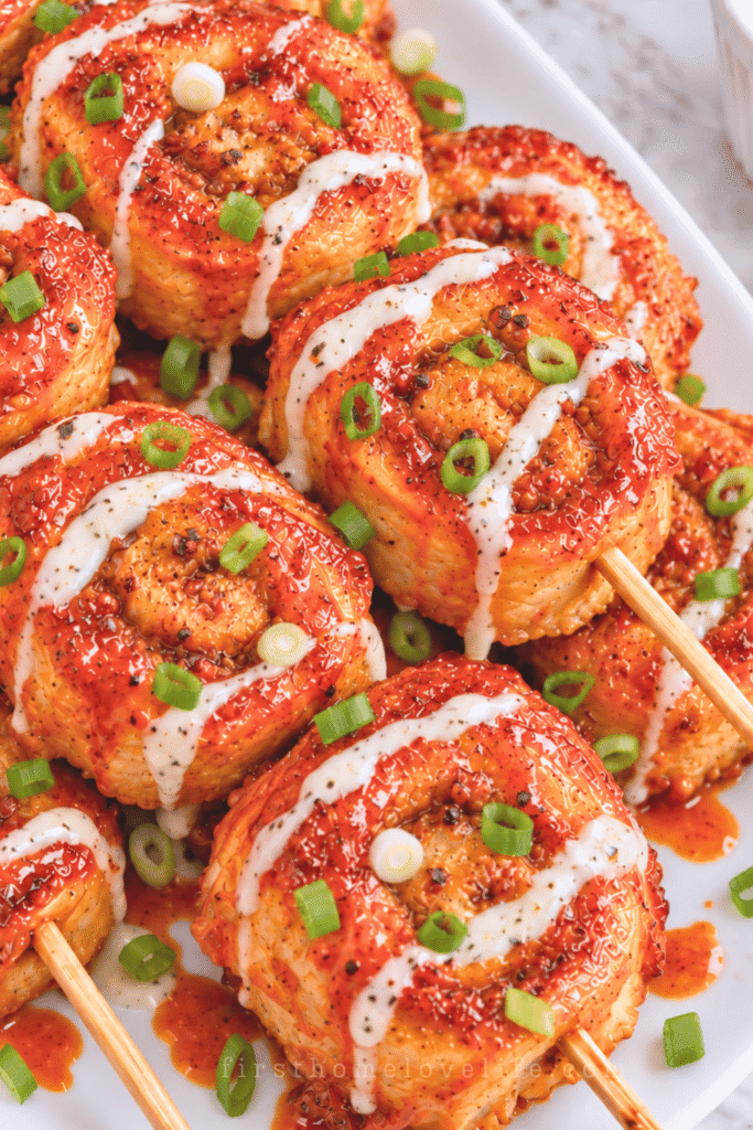 Fried Nashville hot chicken pinwheel smash skewers with ground chicken, ranch drizzle, chopped scallions, and spicy hot sauce.