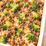 Korean-inspired ground beef and broccoli rice casserole topped with sesame seeds and green onions in a white baking dish.