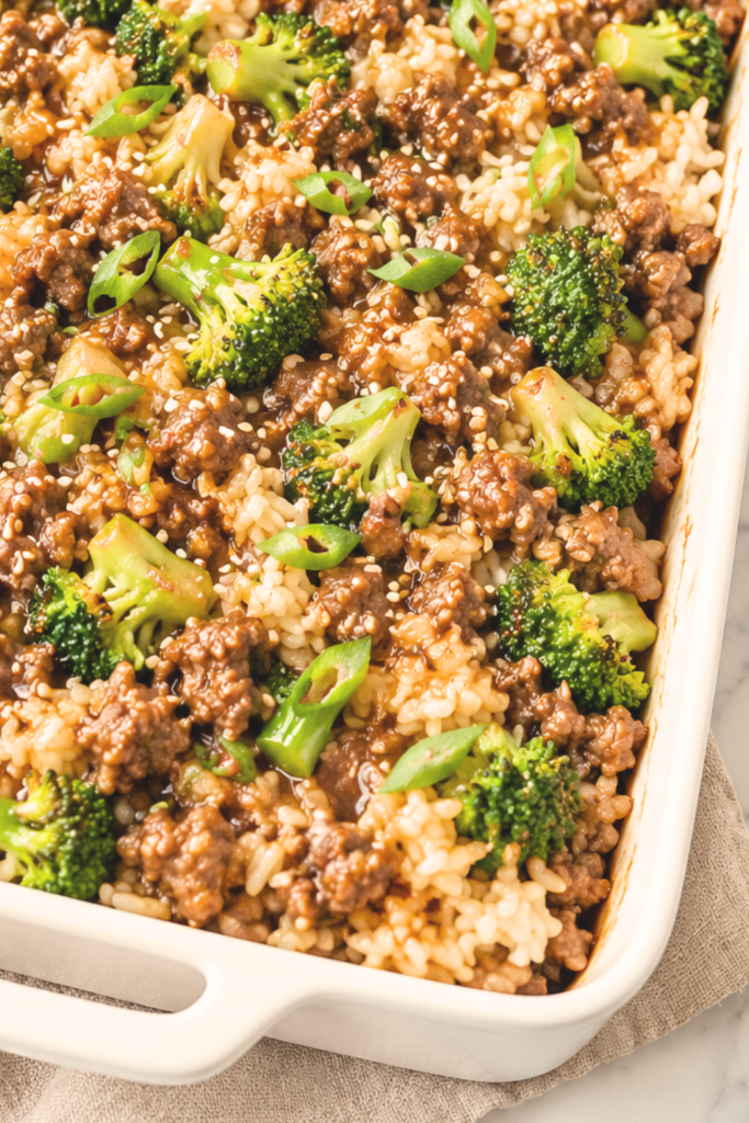 Korean-inspired ground beef and broccoli rice casserole topped with sesame seeds and green onions in a white baking dish.