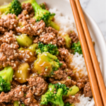 Ground beef and broccoli over white rice with brown sauce and sesame seeds in a white bowl with wooden chopsticks.