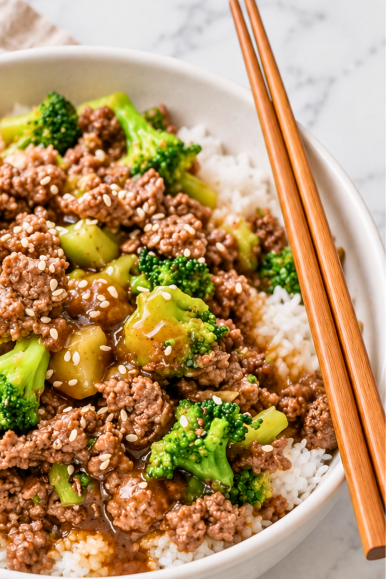 Ground beef and broccoli over white rice with brown sauce and sesame seeds in a white bowl with wooden chopsticks.