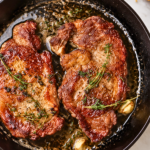 Perfect pan seared steak with garlic herb butter in a cast iron skillet on a white marble countertop.