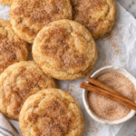 Soft and cakey cinnamon churro cookies coated in cinnamon sugar on parchment paper.