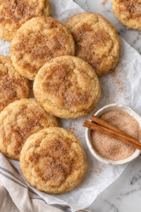 Soft and cakey cinnamon churro cookies coated in cinnamon sugar on parchment paper.