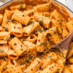 Creamy spicy pumpkin vodka sauce with rigatoni, Parmesan, fresh herbs, and red pepper flakes in a white enamel pan.