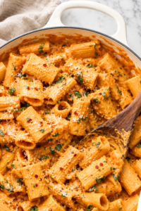 Creamy spicy pumpkin vodka sauce with rigatoni, Parmesan, fresh herbs, and red pepper flakes in a white enamel pan.