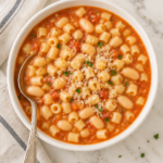 Traditional Italian pasta e fagioli with ditalini pasta and white beans in a tomato broth, served in a white bowl with a silver spo