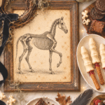 Halloween flat lay with a framed skeleton horse, pumpkins, black candles, spooky treats, moss, ribbon and vintage decor